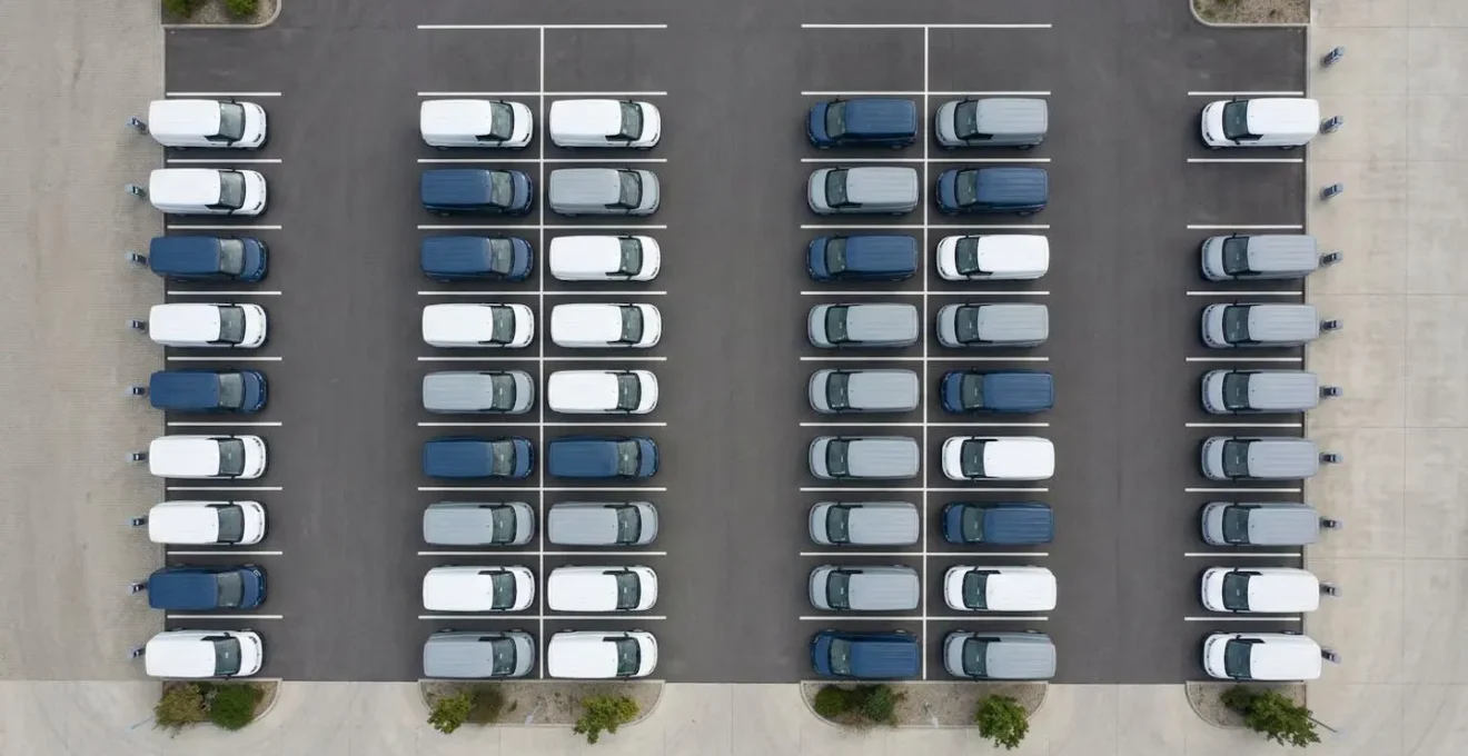 Vue aérienne minimaliste d'un parking d'entreprise avec utilitaires électriques et bornes de recharge